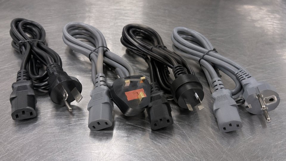 Assorted IEC 60320 C13 power cables with different regional wall plugs laid out on an industrial workbench