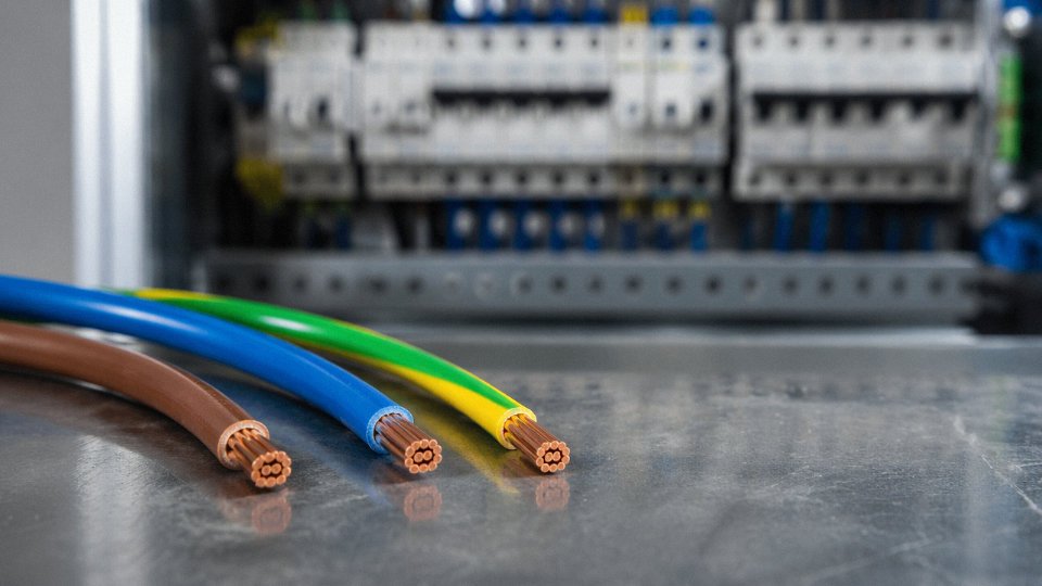 Three electrical wires — live, neutral, and ground — with color-coded insulation laid out side by side on an industrial workbench