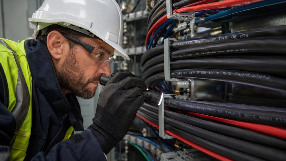 Electrician reading printed identification codes on electrical cable jackets in an industrial panel room